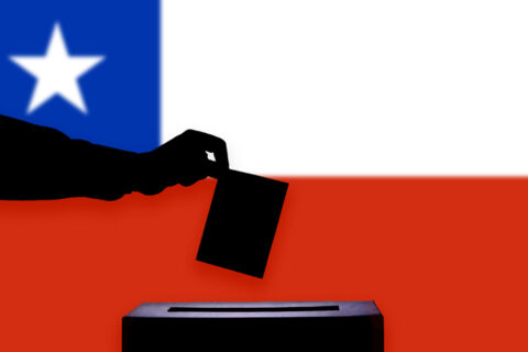 mano metiendo un voto con la bandera chile de fondo